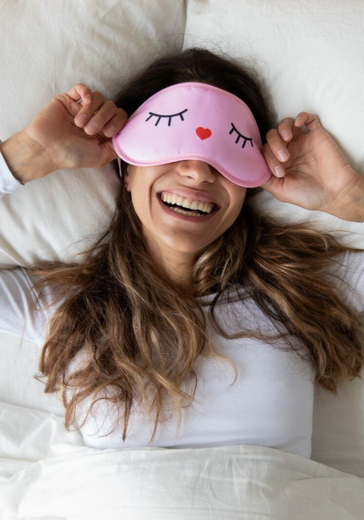 Happy millennial woman lying in bed with sleeping mask | Bow Family Furniture & Flooring